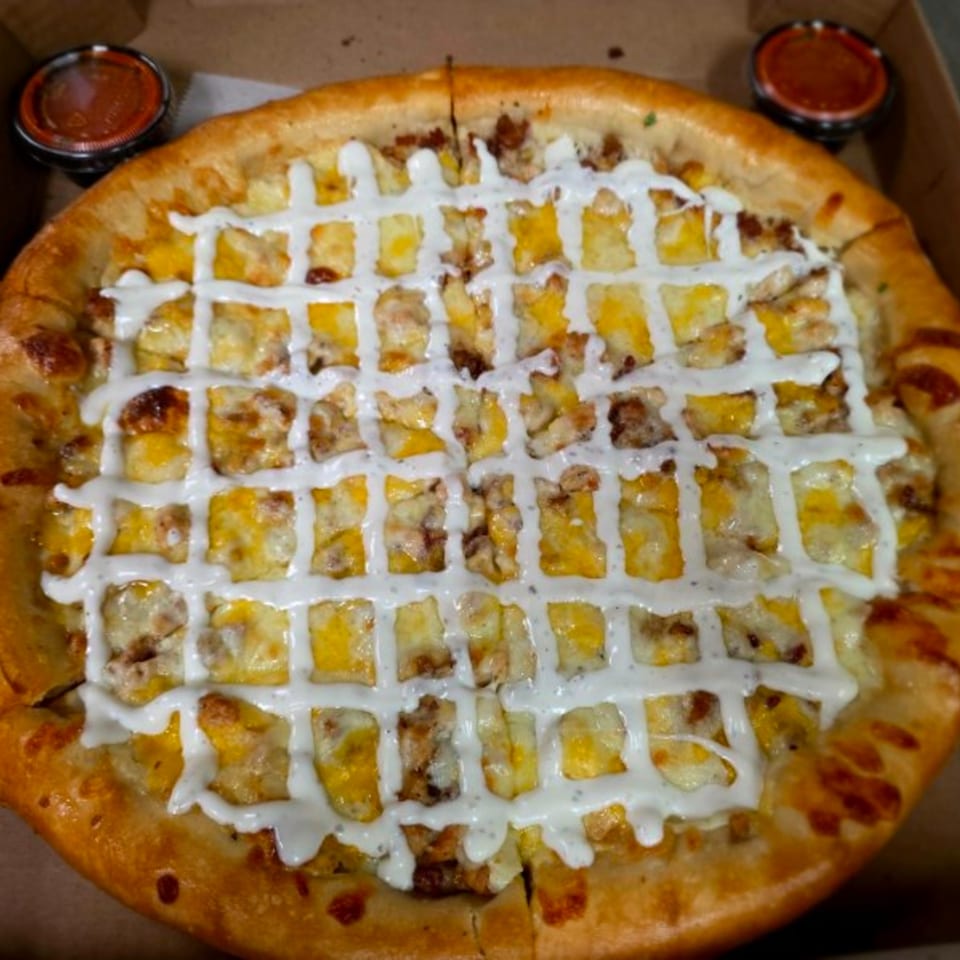 A Buona Cucina Italiano pizza with white sauce drizzled in a grid pattern over cheese and meat.