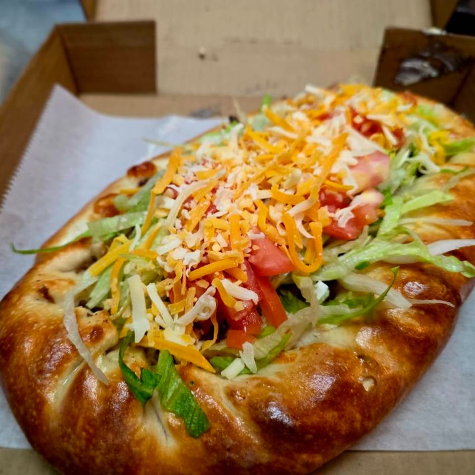 A calzone from Buona Cucina Italiano, topped with shredded lettuce, diced tomatoes, and cheese.