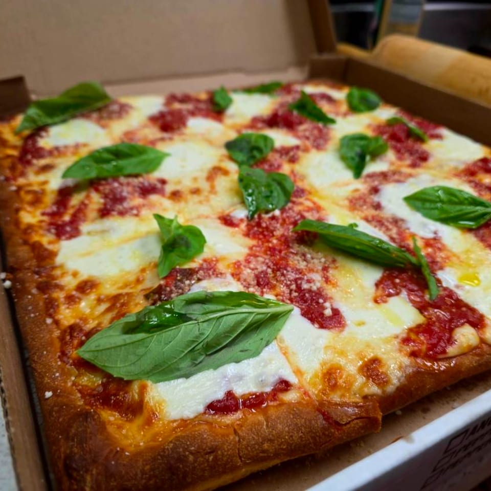 A square Buona Cucina Italiano pizza with melted mozzarella, red sauce, and fresh basil in a box.